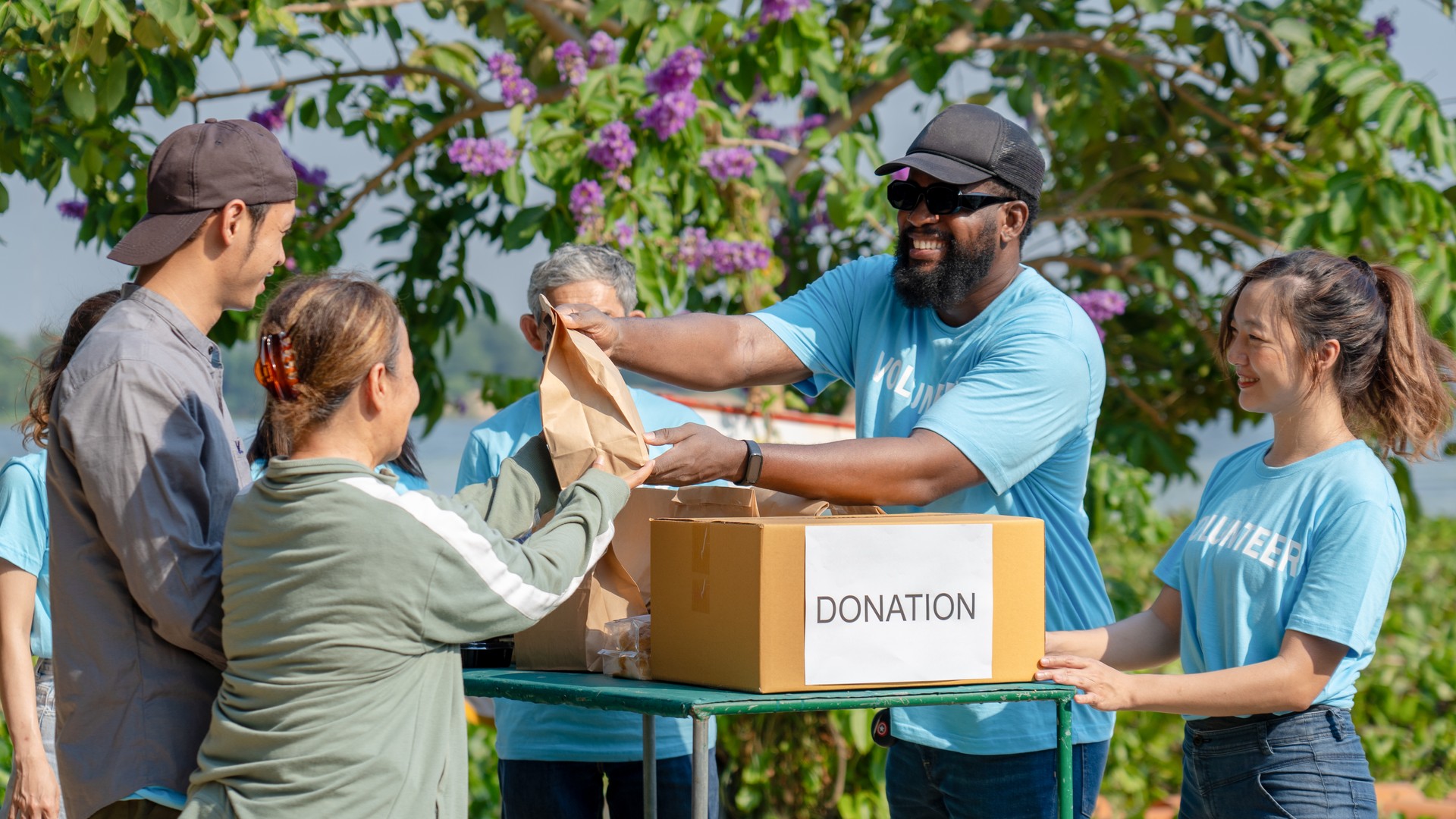 African man volunteer give some food in paper bag to poor people, raising money through donation box