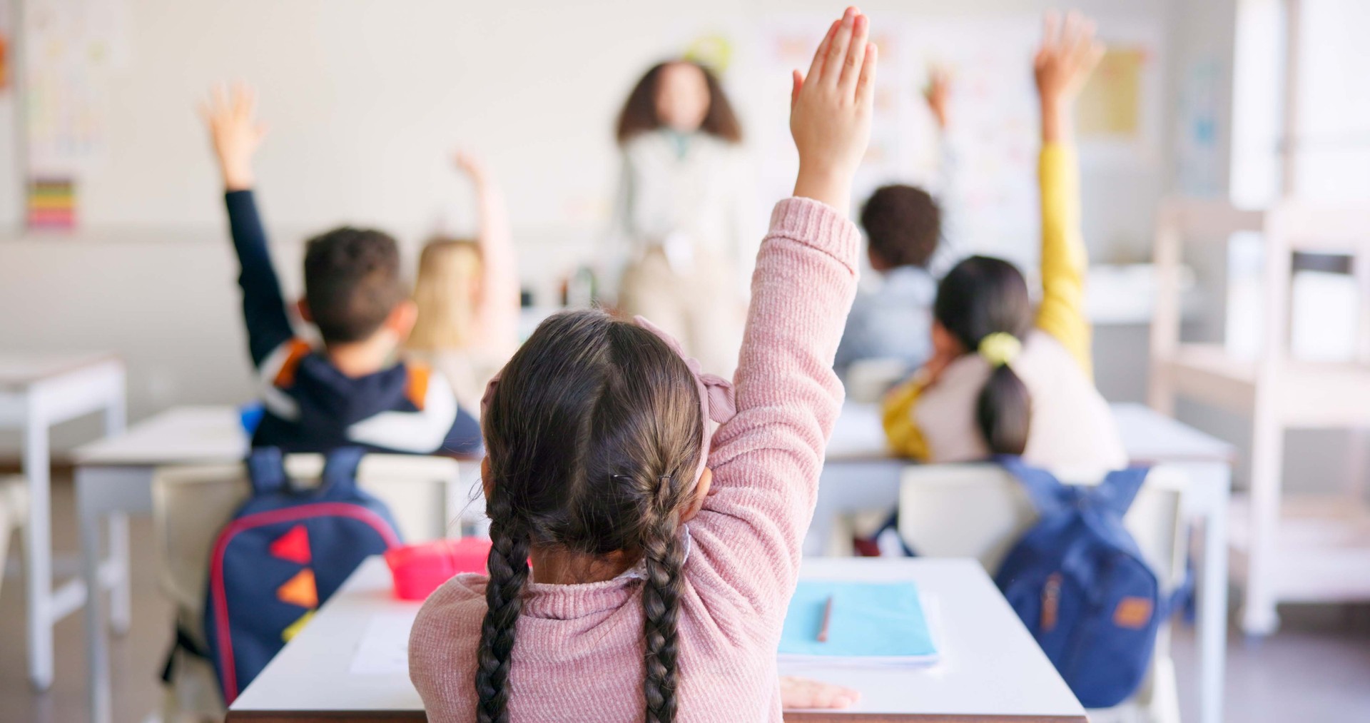 Education, raised hand and girl student in classroom with teacher for learning, discussion and knowledge. Help, studying and children students with questions for female educator or tutor at school.